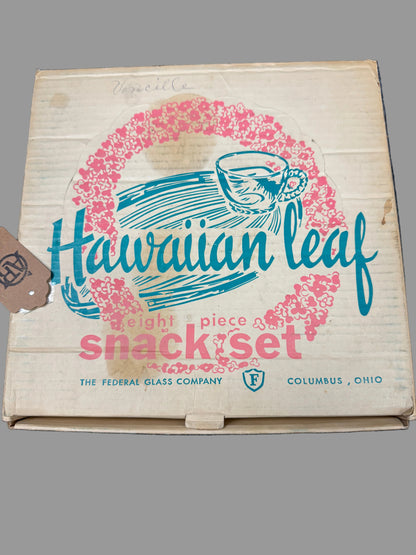 Vintage cardboard box for a Hawaiian Leaf eight-piece snack set by The Federal Glass Company, featuring a pink floral wreath and blue script logo on a beige background, photographed on a dark textured surface.