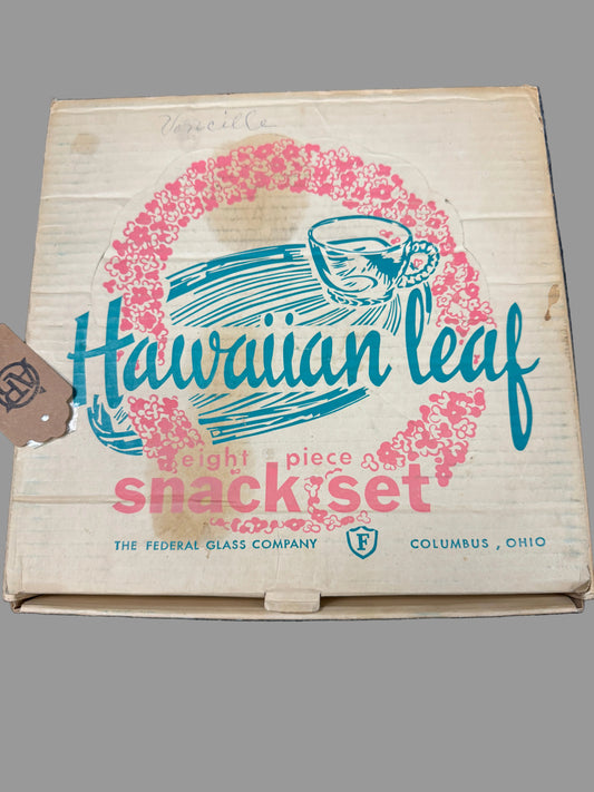Vintage cardboard box for a Hawaiian Leaf eight-piece snack set by The Federal Glass Company, featuring a pink floral wreath and blue script logo on a beige background, photographed on a dark textured surface.