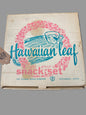 Vintage cardboard box for a Hawaiian Leaf eight-piece snack set by The Federal Glass Company, featuring a pink floral wreath and blue script logo on a beige background, photographed on a dark textured surface.