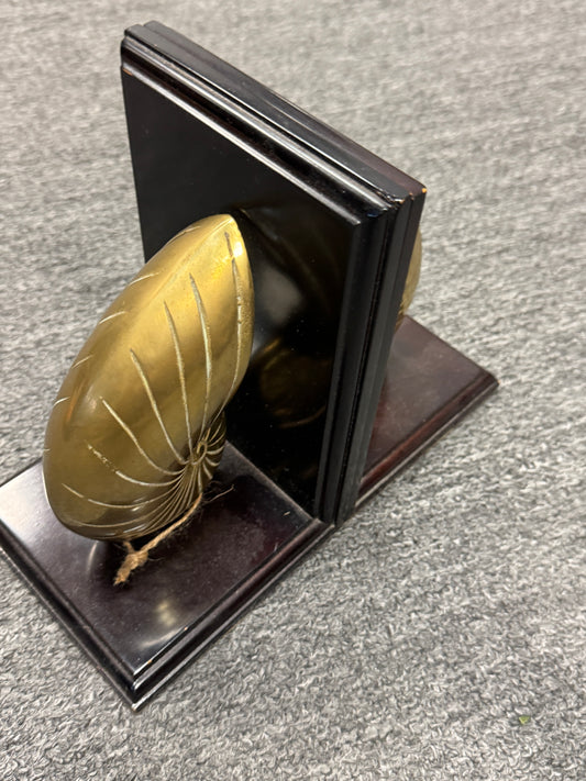 A decorative pair of bookends featuring polished gold-toned leaf-shaped tops and dark brown wooden bases, shown standing on a gray carpeted floor.