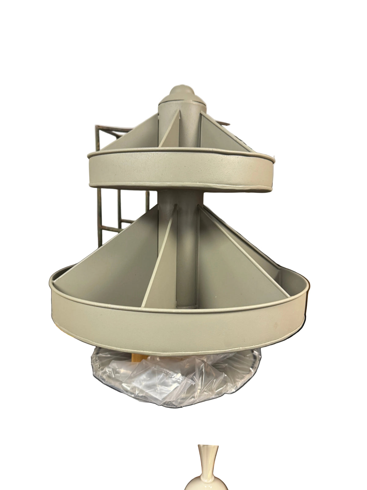 A light gray plastic kitchen accessory, likely a strainer basket or filter cone, resting on a black utility table in a storage room with cardboard boxes in the background.