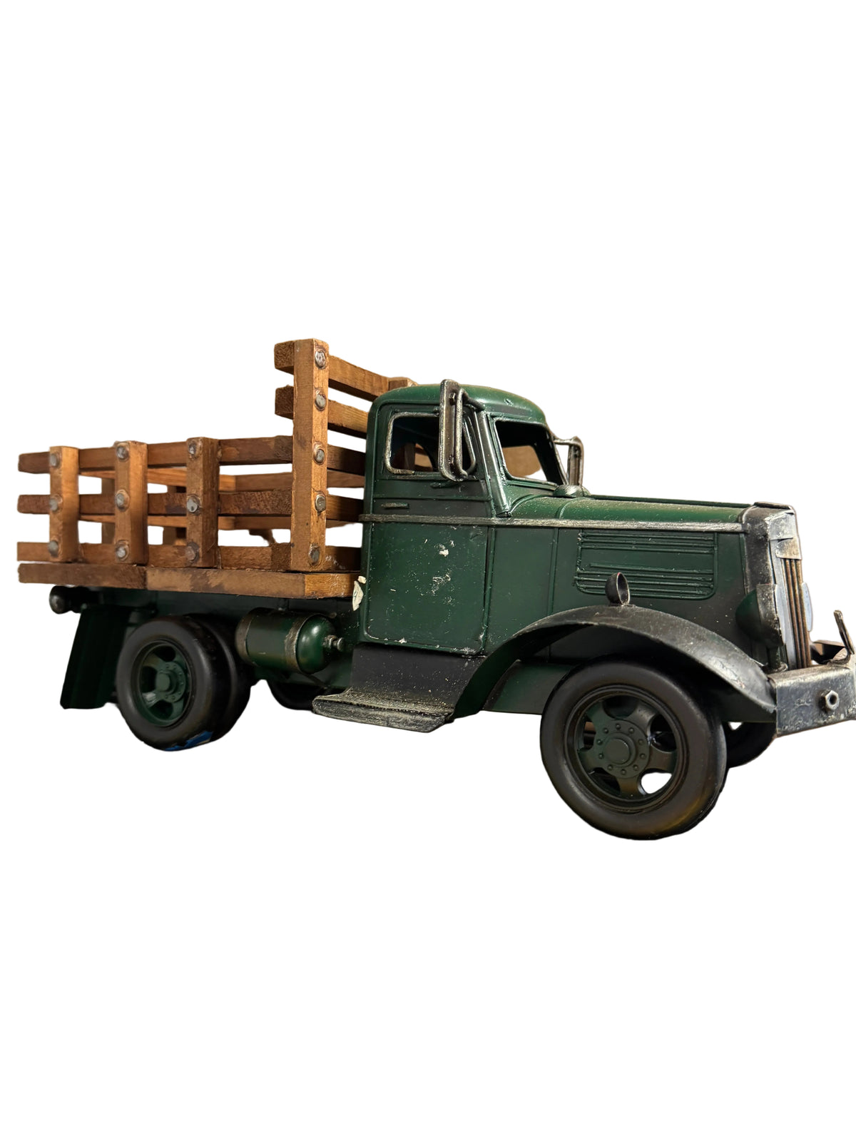 A vintage-style green pickup truck model with a wooden slatted bed, displayed on a yellow shelf in front of a large cardboard box.